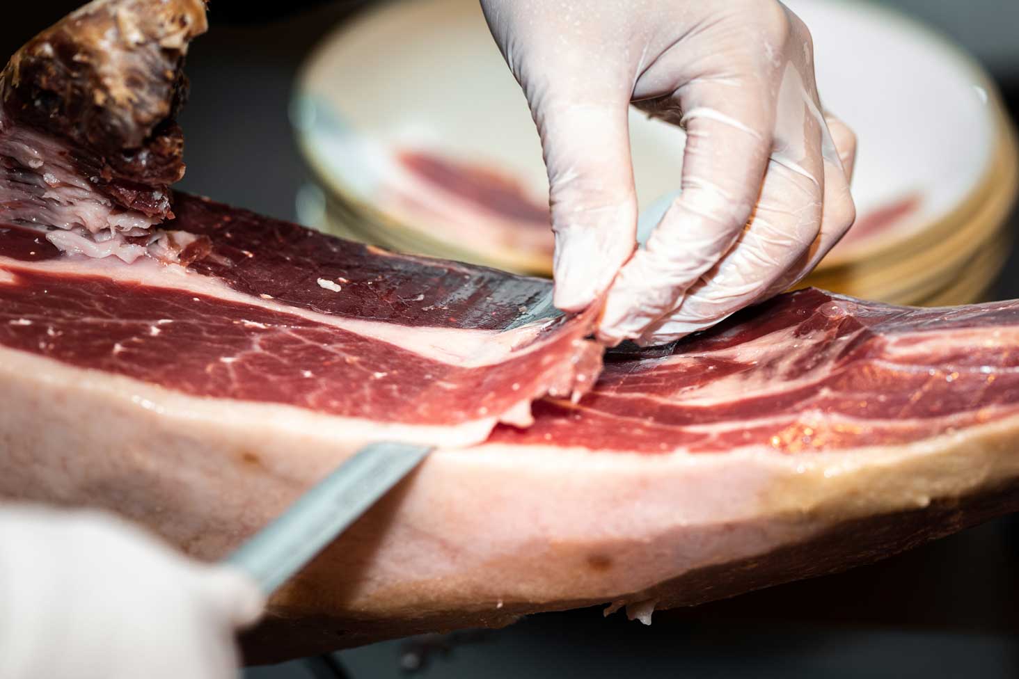 Primer plano de corte a cuchillo de finas lonchas de jamón ibérico con puntos blancos (tirosina)